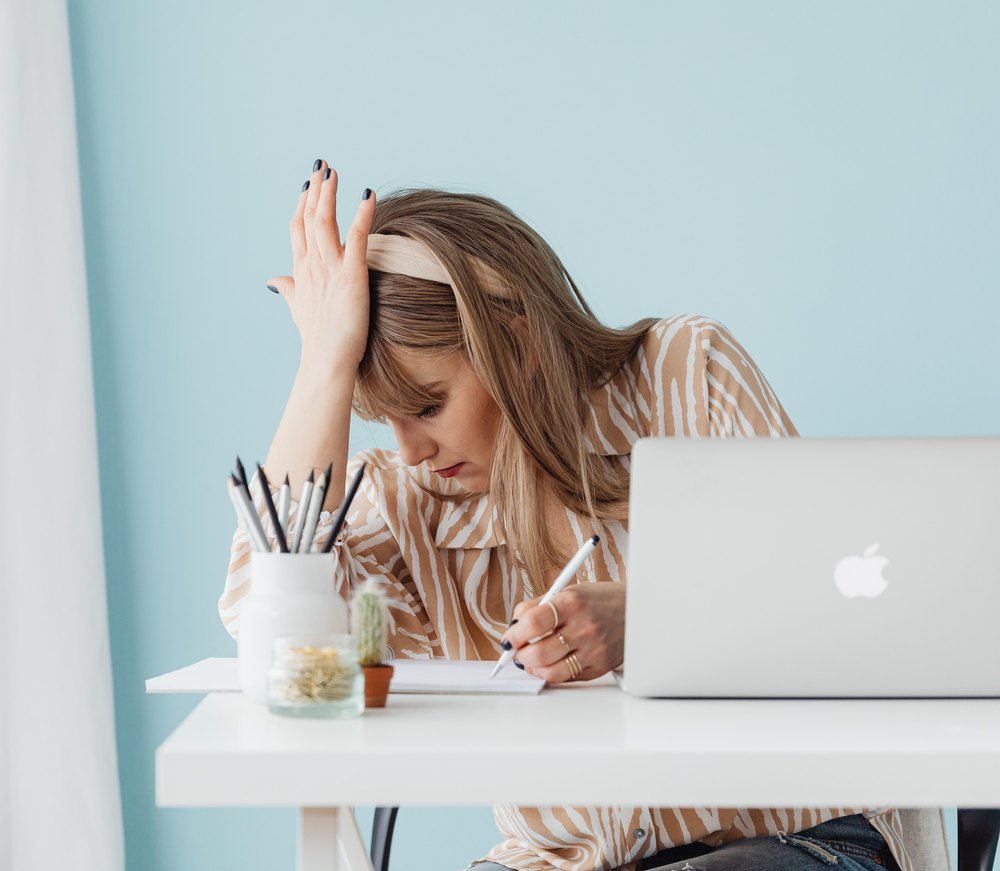 A woman at a desk with a laptop, one hand on her head.